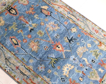 May include: A rectangular area rug featuring a blue field with a multi-colored floral and vine pattern in shades of orange, green, cream, and dark blue. The rug has a detailed border with geometric and botanical motifs throughout the design.