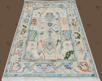 May include: A rectangular rug with a cream-coloured central field and a light blue border. The rug features a central medallion design with floral and geometric patterns in shades of blue, green, and peach. The rug's design is symmetrical and detailed.