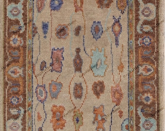 May include: A rectangular area rug featuring a beige centre field with scattered abstract shapes in blue, orange, and brown. The rug has a wide dark brown border with light blue and orange floral motifs and a short white fringe on both ends.