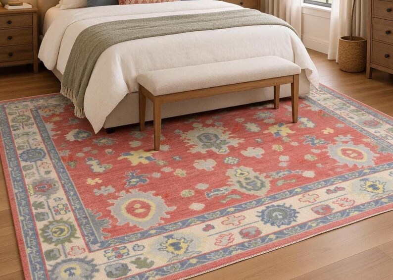 May include: A rectangular area rug featuring a vibrant coral red base with a repeating pattern of stylized floral and geometric motifs in shades of light blue, sage green, and cream. The rug has a wide border with a repeating blue and cream design.