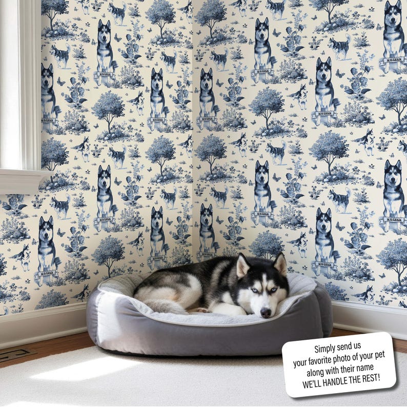 May include: A Siberian Husky dog rests in a gray dog bed in a room with blue and white dog-themed wallpaper. The wallpaper features illustrations of Huskies, trees, and floral elements. Text on the image reads: "Simply send us your favorite photo of your pet along with their name WE'LL HANDLE THE REST!"