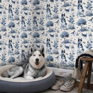 May include: A Siberian Husky dog lounges in a gray dog bed in front of a wallpaper featuring a blue and white toile pattern with Husky illustrations. The wallpaper has trees, butterflies, and the word "Musher" on banners.