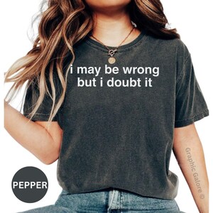 May include: Dark gray t-shirt with the text "i may be wrong but i doubt it" in white. The shirt is a crew neck style and has a slightly faded appearance. The word "Pepper" is in a black circle at the bottom left.