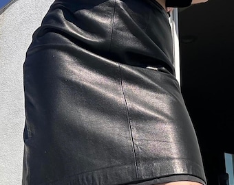 May include: A black leather skirt with a straight, classic silhouette. The skirt appears to be knee-length and has a smooth, shiny texture. The garment is shown in natural light.