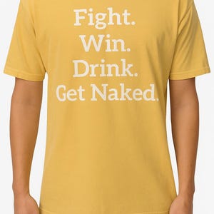 K&ouml;nnte beinhalten: Senfgelbes T-Shirt mit dem wei&szlig;en Aufdruck "Fight. Win. Drink. Get Naked." in Blockbuchstaben. Das Shirt hat einen Rundhalsausschnitt und kurze &Auml;rmel.