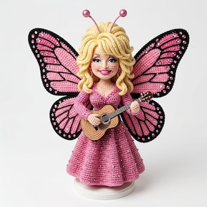 May include: A crocheted doll featuring blonde hair, pink butterfly wings with black borders and rhinestones, and a pink dress. The doll holds a small brown acoustic guitar and has two pink antennae on its head, standing on a circular white base.