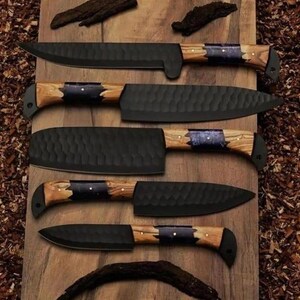 May include: An assortment of five black chef knives with wooden handles and dark metal blades. The knives are arranged on a wooden surface, showcasing their varying blade shapes and handle designs. The handles feature a dark blue accent.