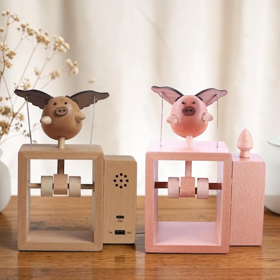 A hand-crafted wooden pig that actually flies — kinetic mechanical art meets music box in one absurd, delightful desk piece.