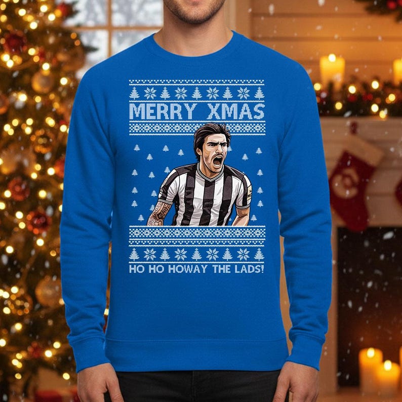 May include: A royal blue Christmas sweater with a festive design. The sweater features the text "MERRY XMAS" above an image of a soccer player in a black and white striped jersey. Below the image is the text "HO HO HOWAY THE LADS!"