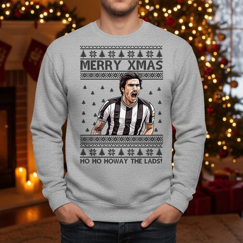 May include: Gray sweatshirt with a festive Christmas design. The graphic features a soccer player in a black and white striped jersey, with the text "MERRY XMAS" and "HO HO HOWAY THE LADS!" in white.
