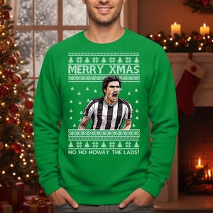 May include: Green Christmas sweater with the text "MERRY XMAS" and "HO HO HOWAY THE LADS!". The sweater features a graphic of a soccer player in a black and white striped jersey. The sweater has a festive design with Christmas trees.