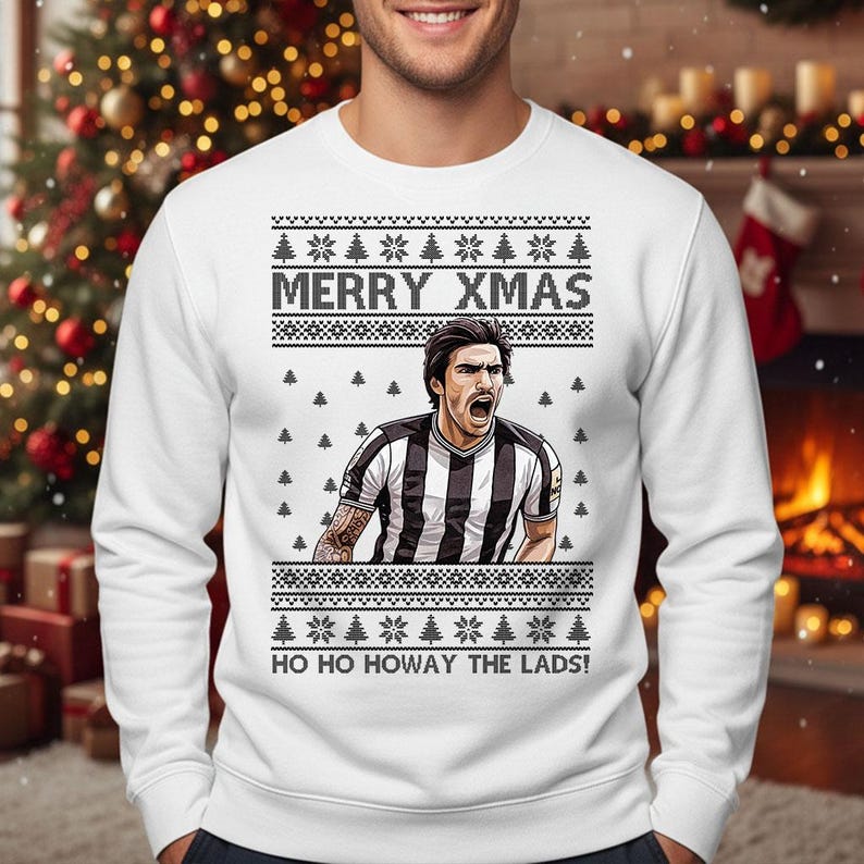 May include: White sweatshirt with a festive design. The sweatshirt features the text "MERRY XMAS" and "HO HO HOWAY THE LADS!" along with a graphic of a soccer player. The design includes snowflakes and Christmas trees.