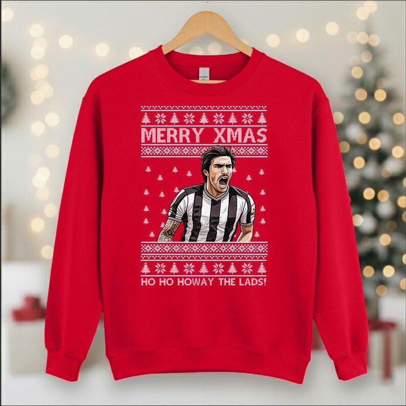 May include: A red Christmas sweatshirt with a festive design. The sweatshirt features a graphic of a soccer player in a black and white striped jersey, with the text "MERRY XMAS" and "HO HO HOWAY THE LADS!"