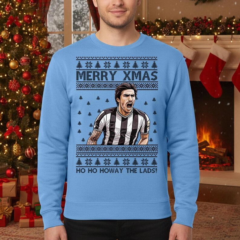 May include: Light blue Christmas sweater with a graphic of a soccer player in a black and white striped jersey. The sweater has the text "MERRY XMAS" and "HO HO HOWAY THE LADS!" in white.