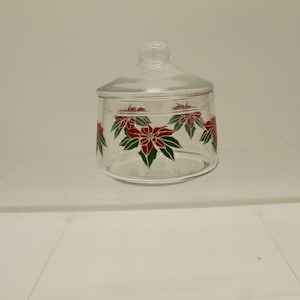 May include: A clear glass jar with a lid, decorated with red poinsettia flowers and green leaves. The jar is perfect for storing cookies, candy, or other treats.
