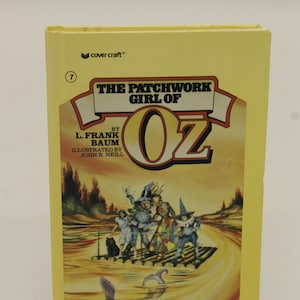 May include: A yellow book cover with the title "The Patchwork Girl of Oz" by L. Frank Baum, illustrated by John R. Neill. The cover features an illustration of characters from the book on a raft floating down a river.