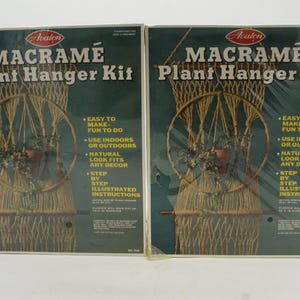 May include: Two identical rectangular boxes for an Avalon Macramé Plant Hanger Kit. The dark green packaging features white text, a logo, and an illustration of a beige macramé plant hanger holding a terracotta pot with a green plant.