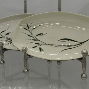May include: Two white oval serving dishes with a green leafy design. The dishes are on a silver stand with three legs.