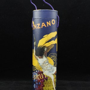 May include: A blue and yellow cylindrical box with a purple rope handle. The box has a vintage illustration of a woman holding a bottle of champagne. The text "BRUT" and "C.INZANO" are visible on the box.