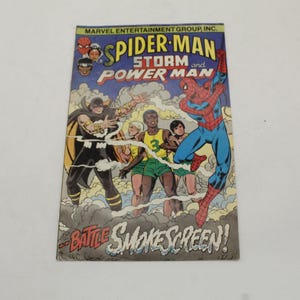 May include: Comic book cover featuring Spider-Man, Storm, and Power Man. The title reads "Spider-Man and Power Man". The artwork depicts a battle scene with characters in action, set against a blue sky and smoky background. The text "Battle Smokescreen!" is also visible.