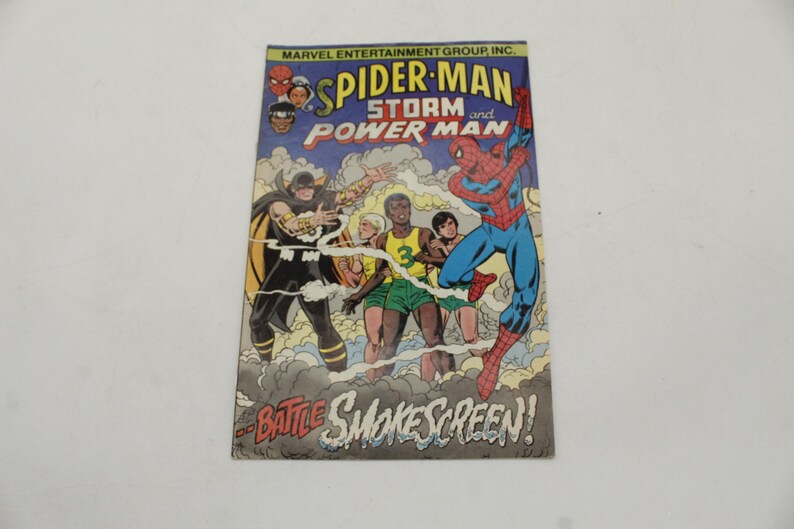 May include: Comic book cover featuring Spider-Man, Storm, and Power Man. The title reads "Spider-Man and Power Man". The artwork depicts a battle scene with characters in action, set against a blue sky and smoky background. The text "Battle Smokescreen!" is also visible.