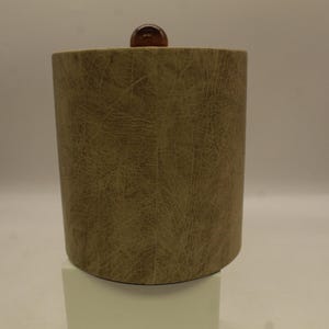 May include: A brown faux leather ice bucket with a wooden top. The bucket is on a white pedestal.