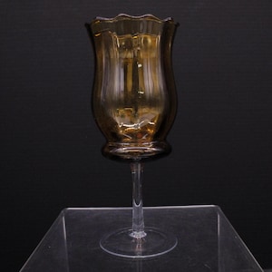 May include: A brown glass vase with a fluted design and a clear glass stem. The vase has a scalloped rim and a round base.