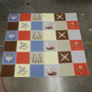 May include: A patchwork quilt with a checkered pattern featuring various designs, including hearts, birds, flowers, and figures. The quilt is made of brown, blue, cream, and red fabric.
