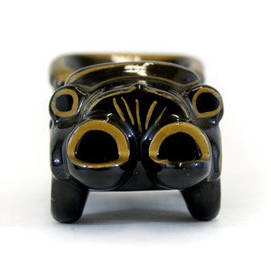 May include: Black ceramic car-shaped trinket with gold accents. The car has a rounded front with two large headlights and a grill.