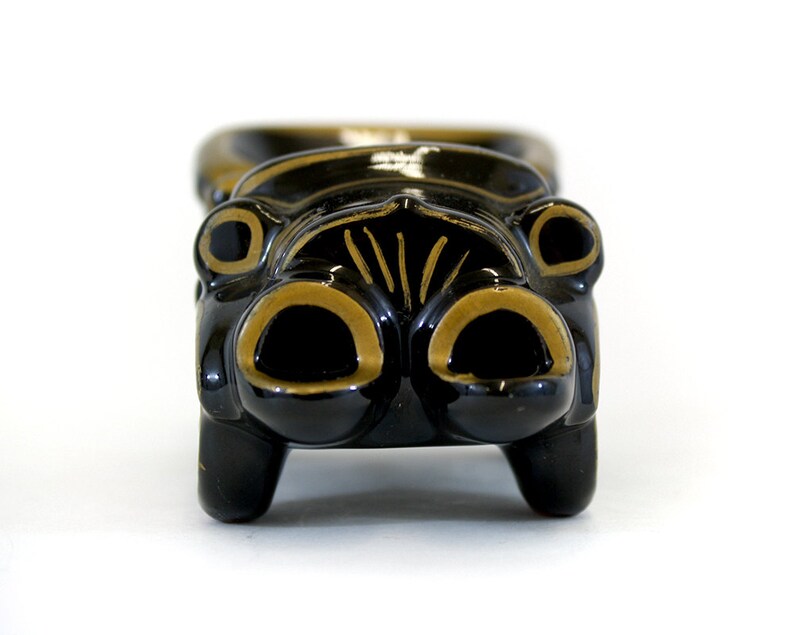 May include: Black ceramic car-shaped trinket with gold accents. The car has a rounded front with two large headlights and a grill.