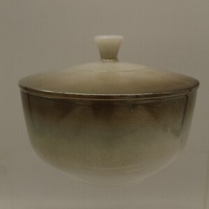 May include: A ceramic bowl with a lid. The bowl is a light brown color with a white rim. The lid has a white knob on top.
