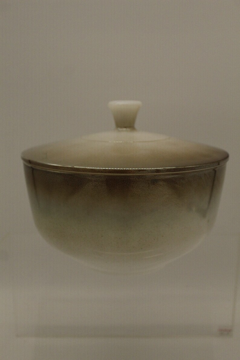 May include: A ceramic bowl with a lid. The bowl is a light brown color with a white rim. The lid has a white knob on top.
