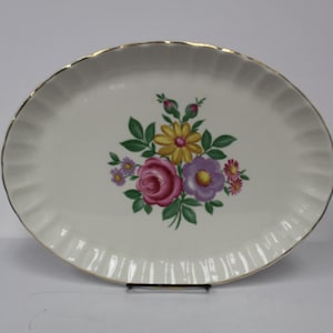 May include: White oval serving platter with a gold rim and a floral design in shades of pink, purple, yellow, and green.