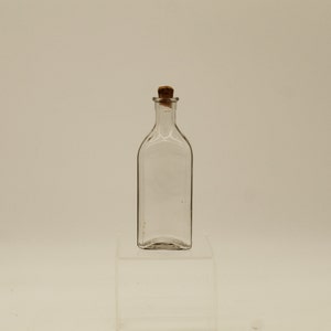May include: A clear glass bottle with a cork stopper. The bottle is empty and has a rectangular shape.