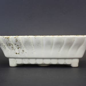 May include: A rectangular white ceramic planter with a scalloped edge and a decorative swirl pattern. The planter has small feet and gold accents along the rim. The planter is approximately 10 inches long.