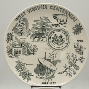 May include: A cream-colored commemorative plate with black illustrations and text. The plate features images of a bear, state buildings, and a cardinal. The text reads "West Virginia Centennial" and "1863-1963".