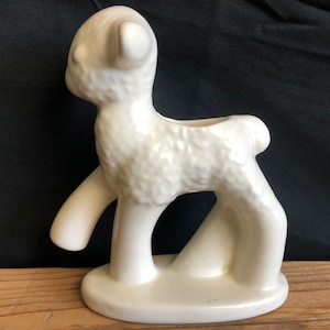 May include: White ceramic planter shaped like a lamb. The planter has a textured surface to resemble wool. The lamb is standing on a base with its head turned to the side.