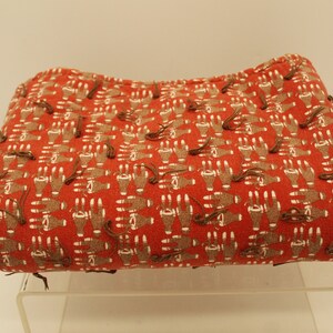 May include: A red fabric with a pattern of brown handprints. The fabric is folded and sitting on a clear acrylic display stand.
