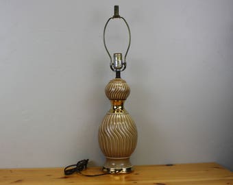 May include: A brown and gold ceramic table lamp with a wavy design. The lamp has a round base and a gold-colored metal shade.