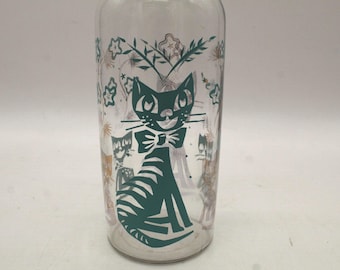 Peut inclure: Un verre transparent orné d'un motif graphique bleu sarcelle foncé représentant un chat portant un nœud papillon. Le design comprend de plus petites illustrations de chats et des motifs floraux dans des tons sarcelle et brun sur le verre.