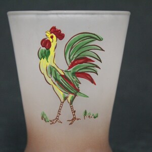 May include: A frosted glass drinking glass with a rooster design. The rooster is yellow, green, and red with a brown outline. The glass has a brown ombre effect at the bottom.