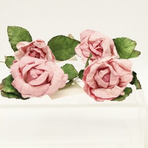May include: Four pink paper roses with green leaves on a clear acrylic display stand.