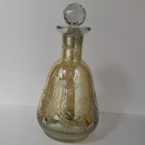 May include: A clear glass decanter with a faceted glass stopper. The decanter is amber in color and has an etched design of grapes and vines.