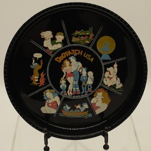May include: A black metal serving tray with a circular design featuring various cartoon characters and the text "Dogpatch USA".