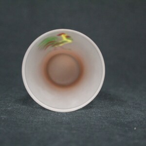 May include: White ceramic cup with a rooster design in yellow, green, and red.