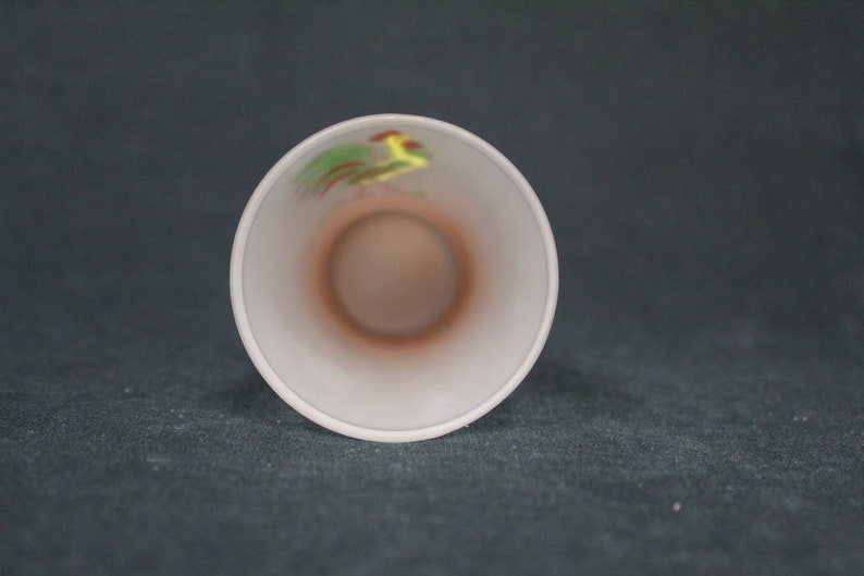 May include: White ceramic cup with a rooster design in yellow, green, and red.