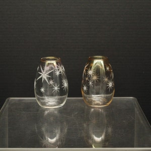 May include: Two clear glass vases with a starburst pattern. The vases have a gold rim and are on a clear glass surface.