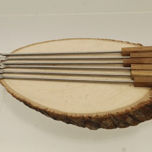 May include: Set of six metal skewers with wooden handles. The handles are decorated with colored dots in red, yellow, blue, and white.