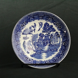 May include: A blue and white porcelain bowl with a traditional Chinese willow pattern. The bowl has a scalloped edge and a raised rim.