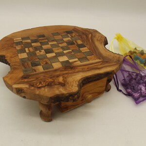 May include: A wooden chessboard set with a natural wood finish. The board is made from a single piece of wood with a natural edge. The chess pieces are stored in a drawer underneath the board. The chess pieces are in two small bags, one purple and one yellow.